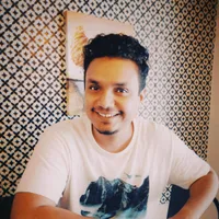 Mannu, smiling, in front of a patterned tiled wall